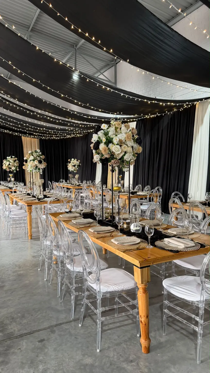 Khan Events reception with long timber tables, clear chairs, floral centrepieces and ceiling draping